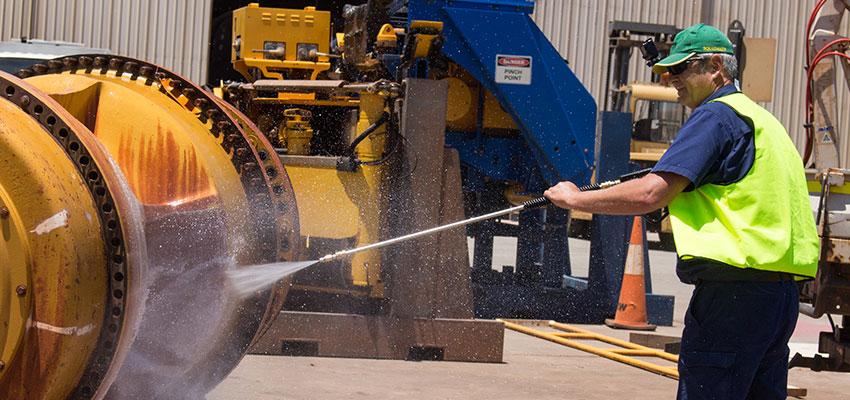 Man using a high-pressure hose to degrease industrial machinery, illustrating LubeLine maintenance and lubrication solutions