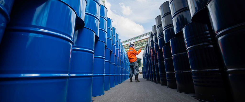 Man walking between rows of stored oil drums in a LubeLine warehouse, illustrating safe industrial storage and handling